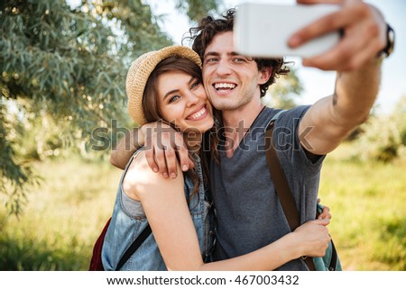 Young smiling happy couple with backpacks hiking in the forest and making selfie