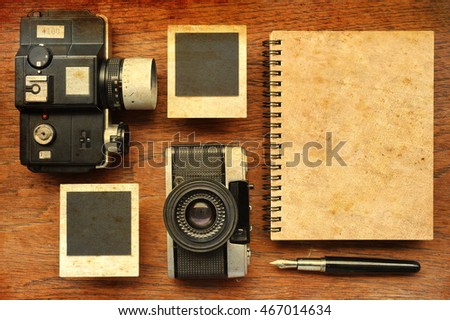 Blank notebook with pen, photo frames and camera on wooden background with sunlight vintage color