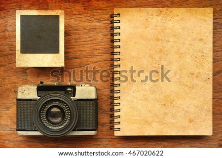 notebook with photo frames and camera on wooden background with sunlight vintage color