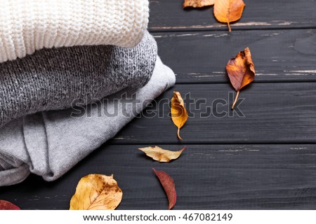 Cozy sweaters and autumn leaves on the black wooden background