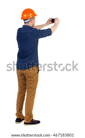 Backview of an engineer in construction helmet stands and using photo camera. Standing young guy. Rear view people collection.  backside view of person.  Isolated over white background. a man in a