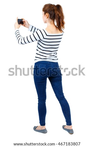 back view of standing young beautiful  woman  using a mobile phone. girl  watching. Rear view people collection.  backside view of person.  Isolated over white background. Girl in a striped sweater