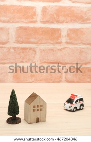 Miniature ambulance and house in front of brick wall.