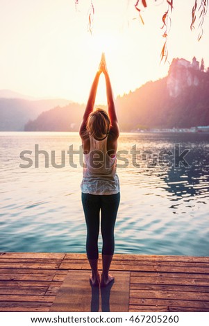 Beautiful woman practicing Yoga by the lake - Sun salutation series - Upward hands pose - Toned image Royalty-Free Stock Photo #467205260