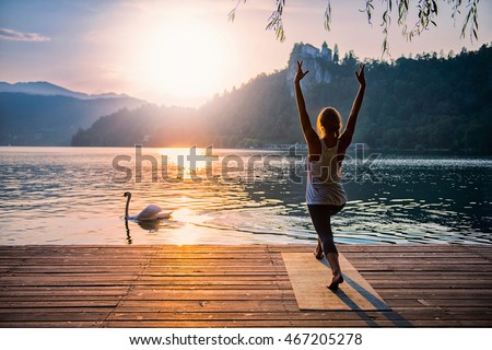 Beautiful woman practicing Yoga by the lake - Sun salutation series - Swan passing by - Toned image Royalty-Free Stock Photo #467205278