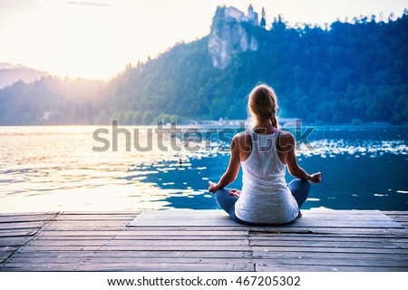 Young woman meditating by the lake Royalty-Free Stock Photo #467205302