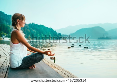 Beautiful woman in lotus position, meditating by the lake, sunset, water birds Royalty-Free Stock Photo #467205314