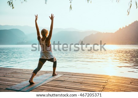 Beautiful woman practicing Yoga by the lake - Sun salutation series - Virabhadrasana - Toned image Royalty-Free Stock Photo #467205371
