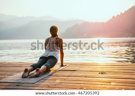 Beautiful woman practicing Yoga by the lake - Sun salutation series - Upward facing dog - Toned image Royalty-Free Stock Photo #467205392