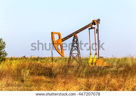 A small private oil derrick pumps oil on the field. The old handicraft oil rig in the background of the creative industrial design. Illegal development of minerals. Bulgaria Tyulenovo, 2016
