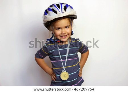 Pretty small girl in bike helmet with gold medal on her neck over white background, cycle sport, indoor portrait, sport and health concept Royalty-Free Stock Photo #467209754