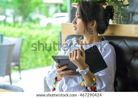 Young woman uses tablet being looking outside green nature while relaxing at home with coffee on the sofa couch