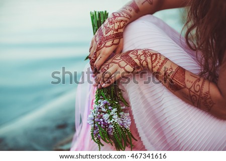 Lady's hands with henna tattoos hold violet bouquet