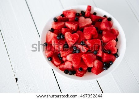 Fresh juicy watermelon slice with cut out heart shape, filled fresh berries, on plate, on wooden background