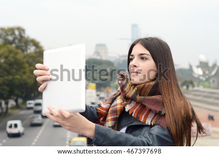 Portrait of a young beautiful woman taking selfie with her tablet. Outdoors. Urban scene.