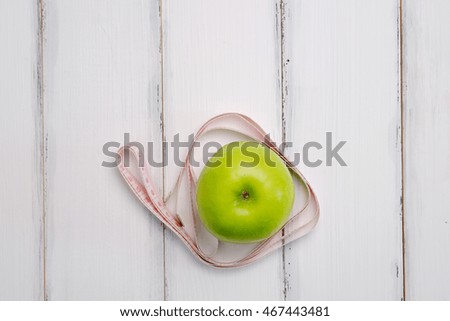Green apple and measuring tape concept on white wooden table background. Top view with copy space.