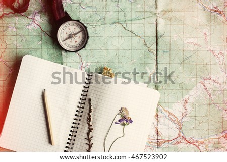 wanderlust and adventure concept, compass and notebook with wildflowers and pencil on map, top view, vintage toned image, space for text
