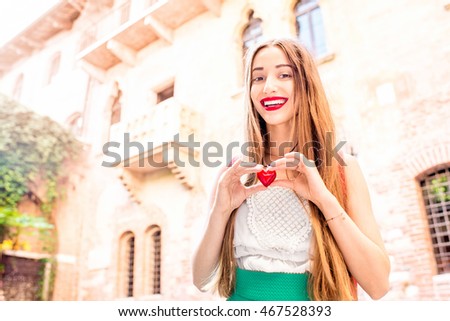 Beautiful woman holding decoration in the form of heart near Romeo and Juliet balcony in Verona.