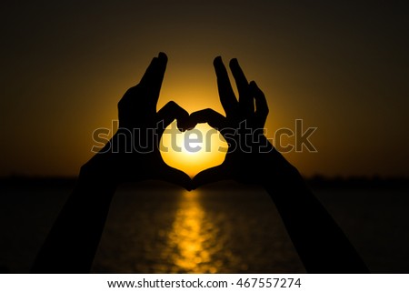 Concept or conceptual heart shape or symbol of human or woman and man hand silhouette over sky and sea at sunset background, for love, valentine, romantic, couple, wedding, romance, summer or sunrise