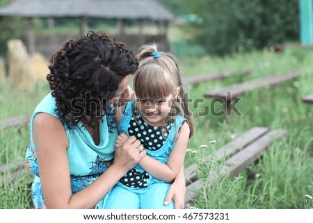 cheerful young mother plays with her little daughter in the meadow on the street in summer