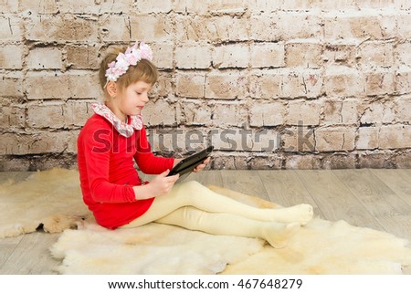 Little Girl with Tablet Computer on White Wall Background. Education works on the tablet for children. Children and computer technology.