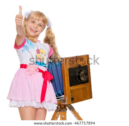 Beautiful little girl with long blonde ponytails on the head posing with an old camera. The girl held out her hands raised in the Upper thumb . Gesture all is well-Isolated on white background