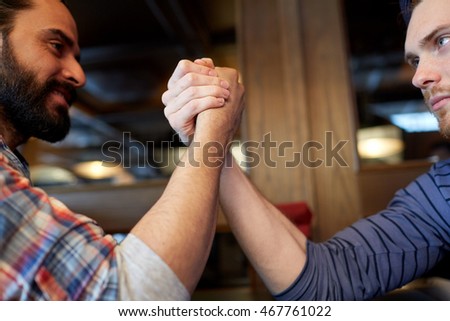 people, leisure, challenge, competition and rivalry concept - close up of male friends arm wrestling at bar or pub