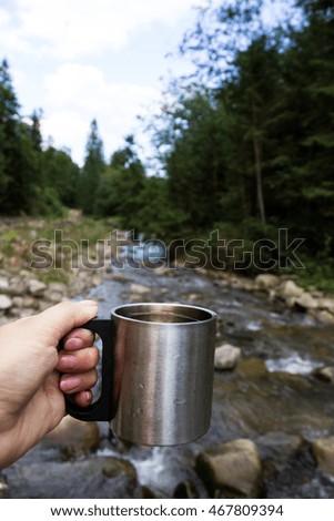 Metal travel mug stands on a log on the background of a mountain river