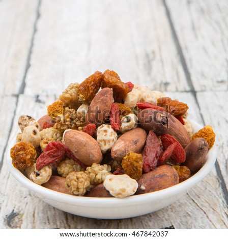 Mix dried super food tiger nuts, mulberry berries, cacao beans, goji berries, golden berry in white bowl over wooden background