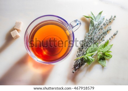Picture of glass cup with tea, herbs and sugar on marble surface.