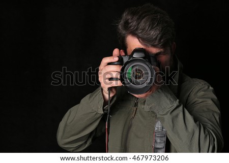 Photographer looking into the camera takes picture. Close up. Black background