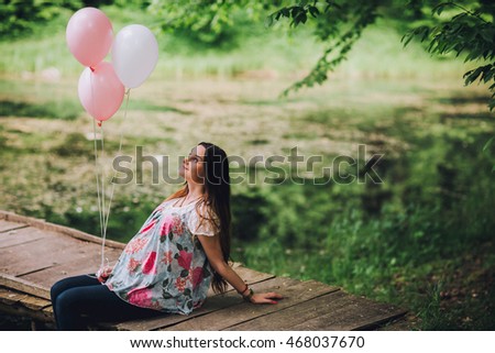Young beautiful pregnant woman relaxing at the lake. Pregnacy with baloons on pier. Forest background. 
