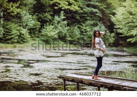 Young beautiful pregnant woman relaxing at the lake. Pregnacy with baloons on pier. Forest background. 