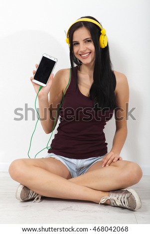 People, leisure and technology concept - happy woman or teenage girl in headphones listening to music from smartphone and dancing at home