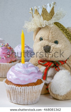 Cupcakes with a candle on the first birthday of a little girl. Against the background of a teddy bear with a clip in the form of a crown.