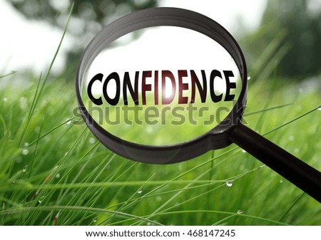 Magnifying glass with the word confidence on grass background. Selective focus