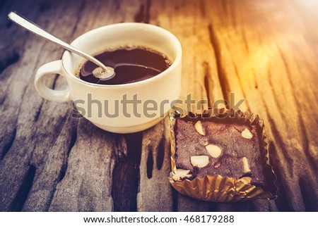 Piece of cake chocolate brownie and hot coffee on old wooden background with bright sunlight. Shallow depth of field (dof), selective focus. High contrast and low key light picture style.