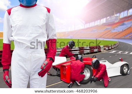 Race car driver posing in front of the pit stop with team maintaining technical service for a racing car during competition event