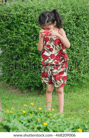 Cute little asian girl having fun taking a photo with a toy camera on green field.