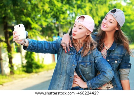 two girls friends or sisters have fun outdoor and taking selfie with smartphone