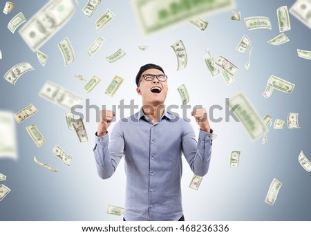 Excited Asian man standing with arm folded in money rain and screaming with joy. Concept of sudden enrichment