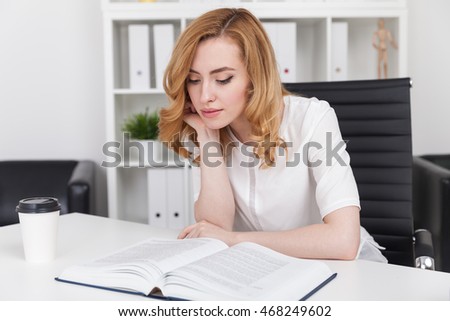 Girl in office reading big book. Office interior in background. Concept of imaginary world and escape from reality