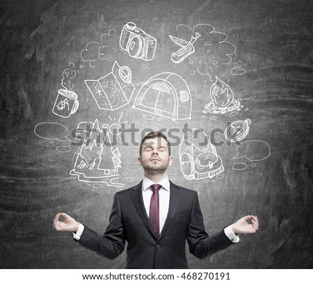 Young man meditating against black board with travel sketches pictured on it. Concept of need of rest and relaxation