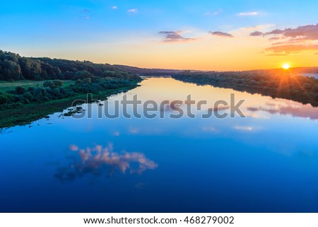 sunset on the river embankment at summer evening with clouds and trees