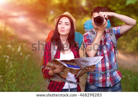 Boy and Girl in sporty and travel Clothing searching Map and taking Photo of wild Nature