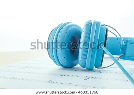 Selective focus blue headphone on music note paper on white background with copy space.