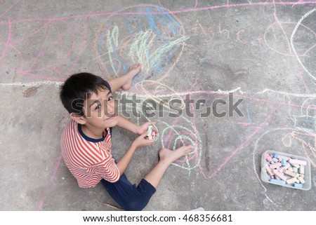 Little boy drawing and coloring by chalk on the ground 