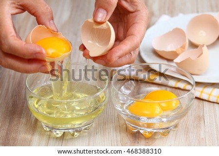 Woman hands breaking an egg to separate  egg white and  yolks and egg shells at the background   Royalty-Free Stock Photo #468388310