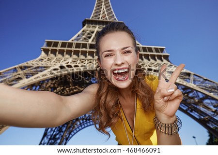 Touristy, without doubt, but yet so fun. happy young woman taking selfie and showing victory against Eiffel tower in Paris, France