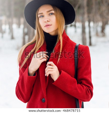 Outdoor fashion portrait of glamour l young  cheerful  stylish lady wearing trendy  winter  outfit , black wool  hat  and red coat . Cold season.Blonde long hair. Full lips, blue eyes.